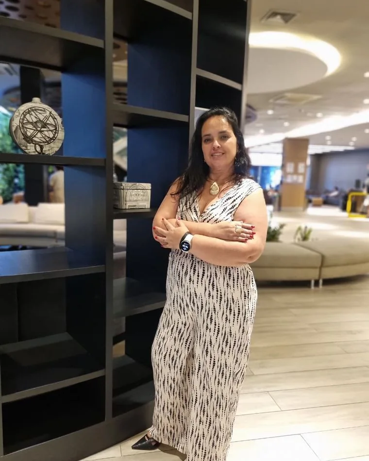 Fernanda Nunes sorrindo, de braços cruzados, ao lado de uma estante
