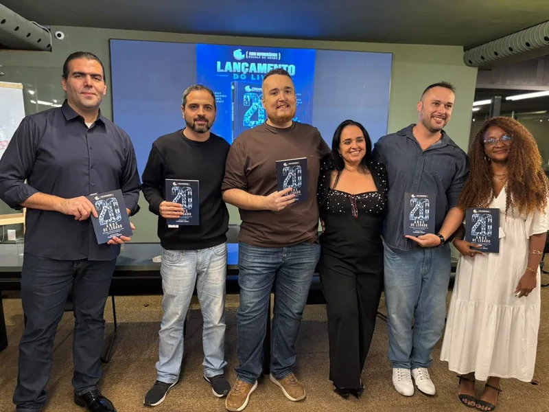 Fernanda Nunes com cinco professores da COTI segurando exemplares do livro 20 Anos de Legado no evento de lançamento